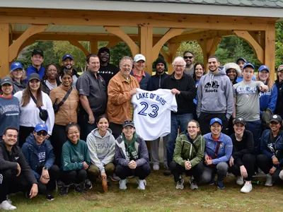 Group photo of the Blue Jays Foundation, Parks Department Superintendent Scott MacKinnon, Township Mayor Terry Glover, and Lake of Bays Township trail maintenance volunteer Doug Ward holding a gifted Blue Jays jersey in the middle.