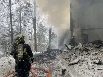 Firefighters extinguish a structure fire with heavy smoke and charred debris in the snow.