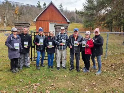 The Heritage Committee and dedicated community members standing in front of Paint Lake Cemetery, holding newly released walking tour brochures.