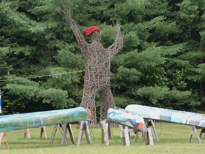 A 19-foot-tall arboreal sculpture situated next to seven canoes with murals painted on them.